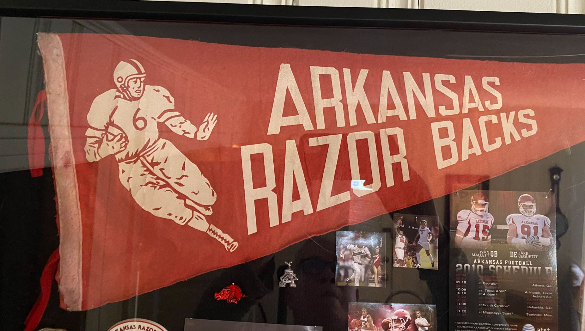 A red pennant with a football player at the widest part and "Arkansas Razorbacks" to its right. There are various U of A athletic photos around it.