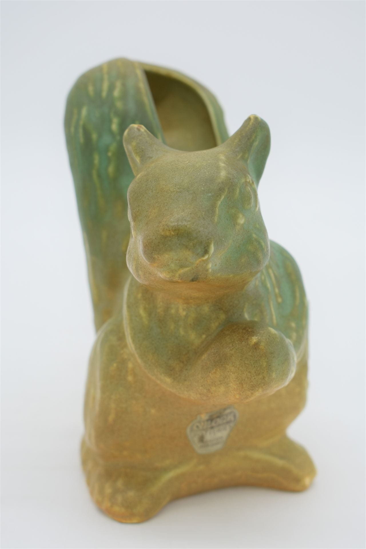 A ceramic vase in the shape of squirrel. The piece is an ombre shade, from dark green at top of head and tail down to yellow at the feet.