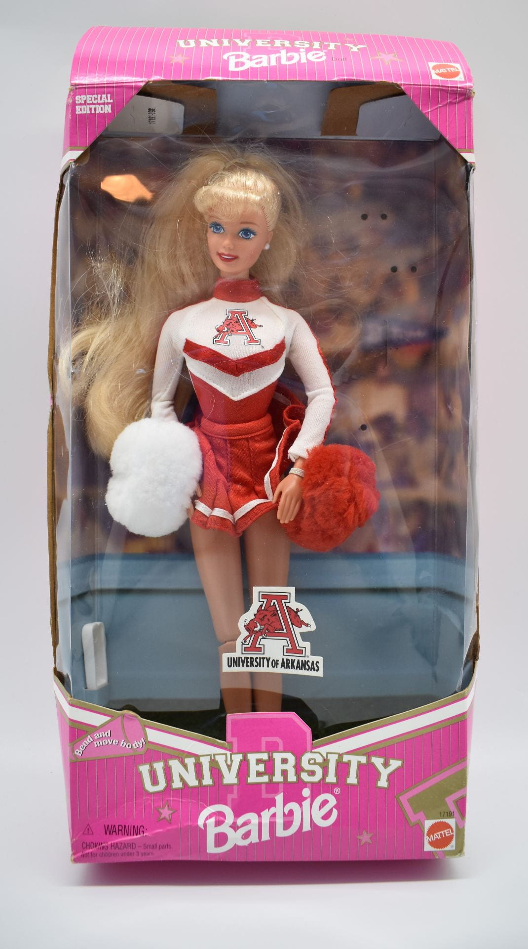 A pink box with a clear front that features a Barbie in a Razorback cheerleader uniform. At the bottom of the box, there is a label that says "University Barbie."