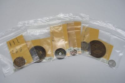 Seven small clear bags, each holding a coin with a small paper insert with identification numbers.