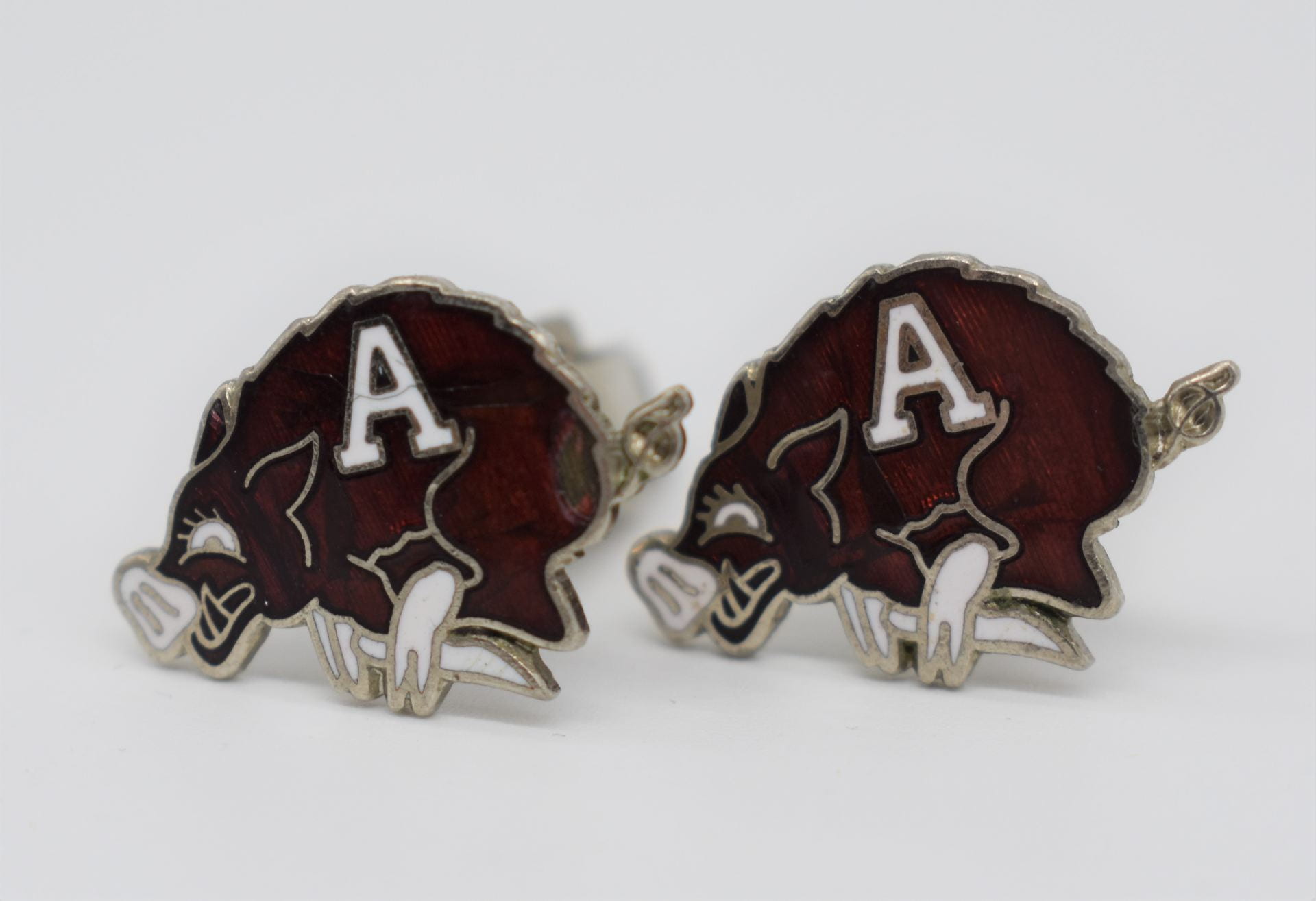 A pair of metal cufflinks in the shape of red Razorbacks with the letter "A" at the center.