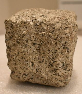 A square chuck of light colored rock with darker specks throughout.