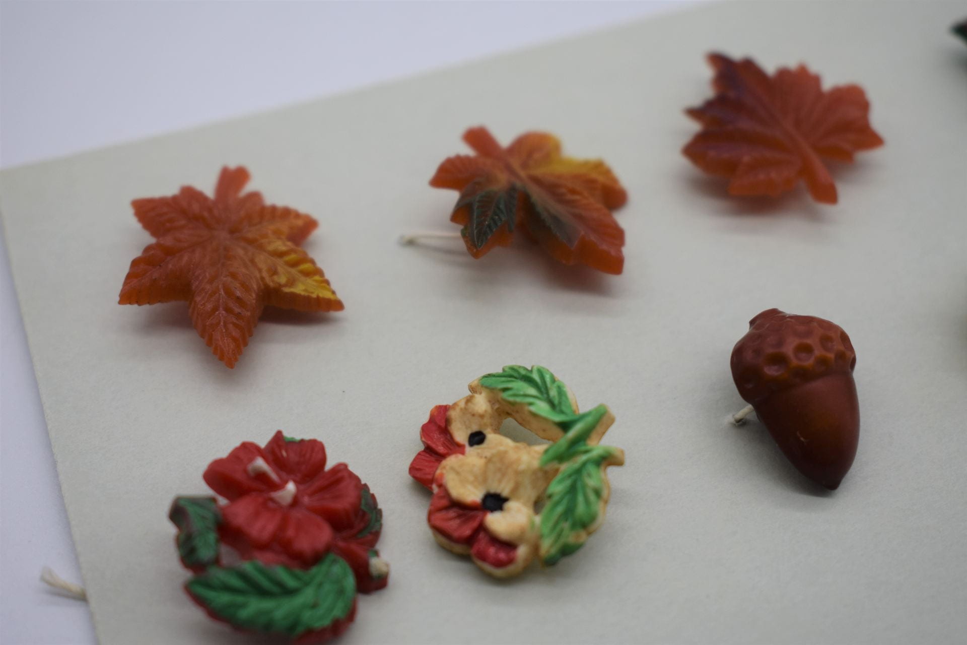 A row of different shaped buttons sewn onto a piece of paper. The buttons include little orange leaves, bouquets of flowers, and an acorn.