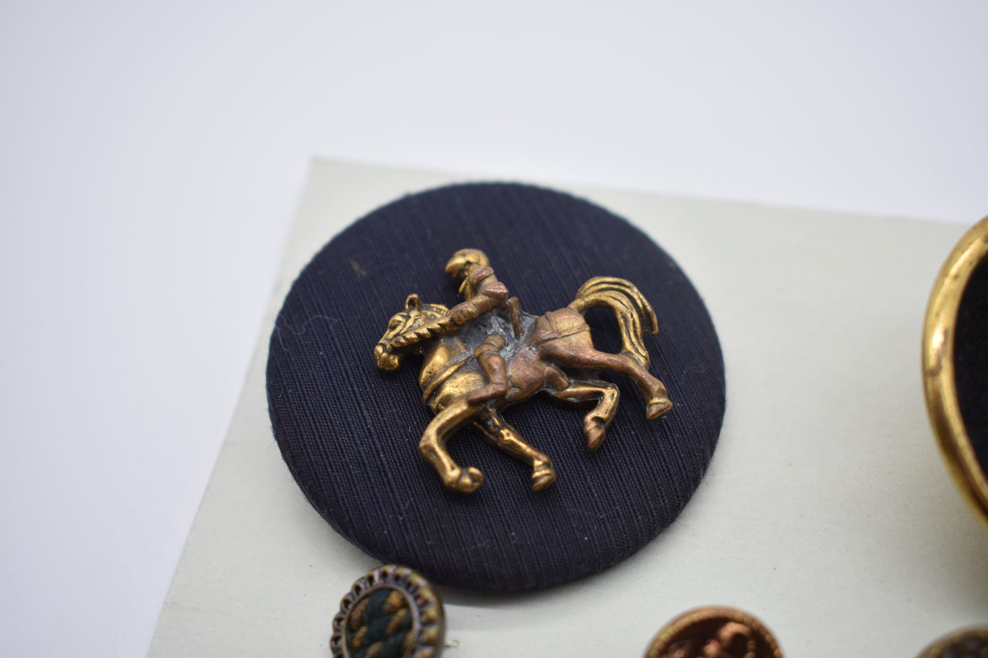 A large black and round button with a raised image of a person riding a horse in gold.