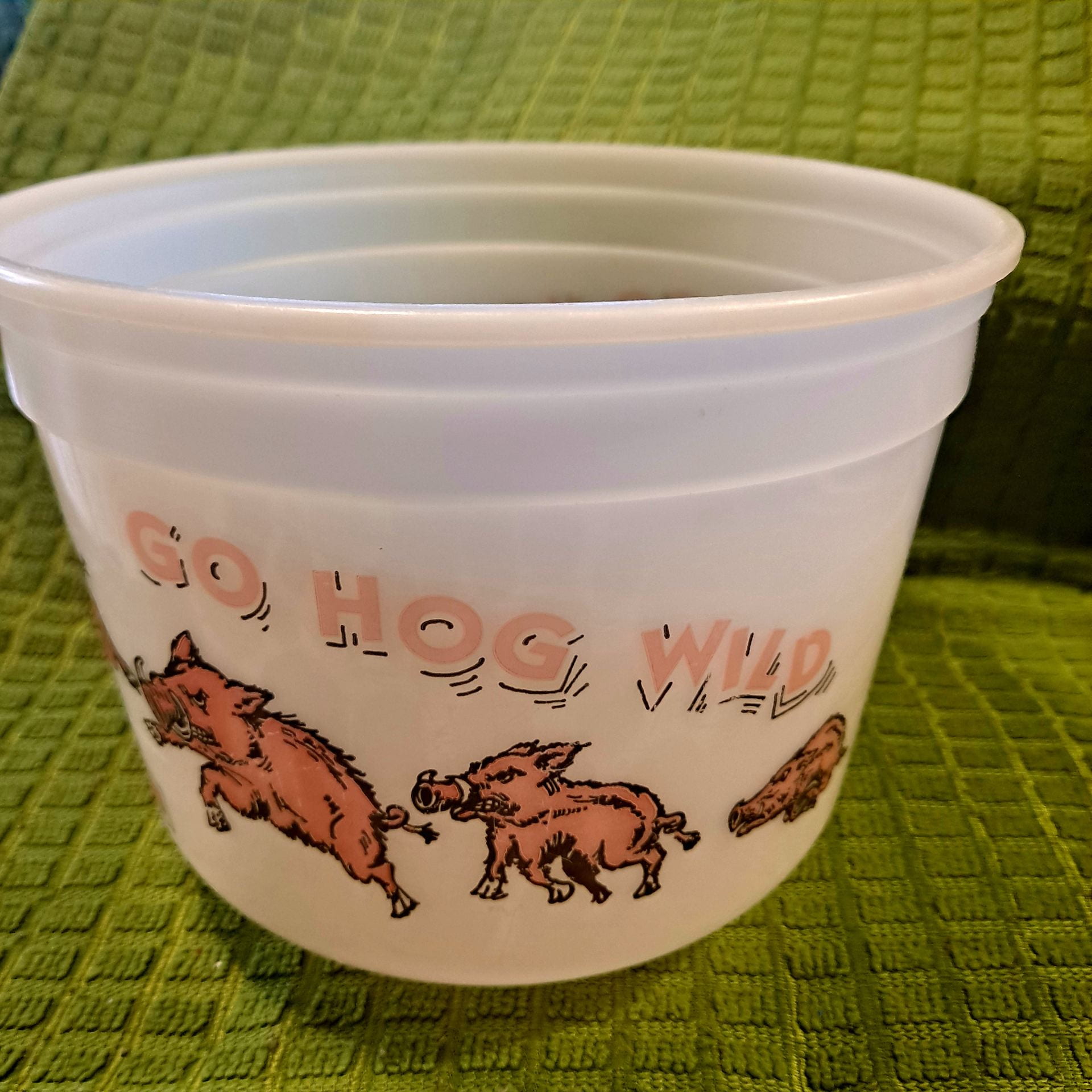 A plastic popcorn container with "Go hog wild" and three hogs running underneath.