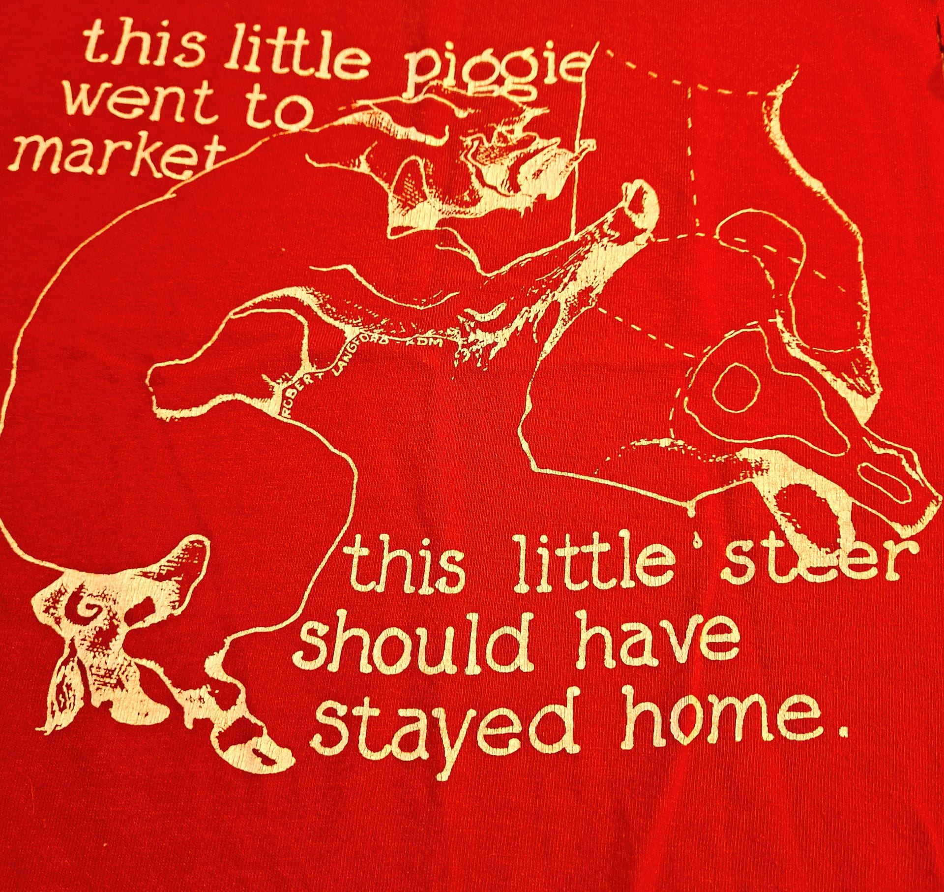 Close-up of a red t-shirt with a pig next to a steer about to be butchered. It says "This little piggie went to market; this little steer should have stayed home."