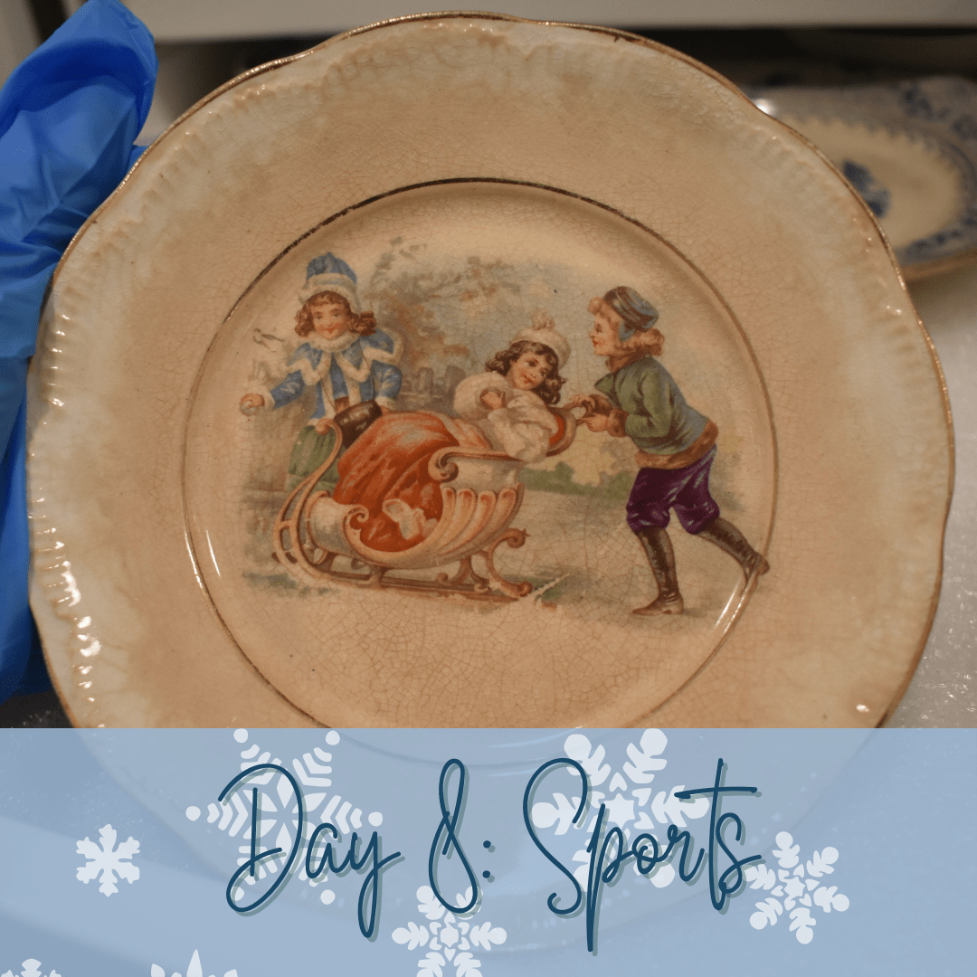 A yellowed plate with a colorful image of three children playing in the snow. One is sitting in a sleigh talking to another behind her. The third child is holding a snowball. A blue banner at the bottom says "Day 8: Sports"