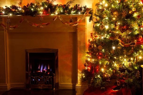 A low lit room with a fireplace and a decorated Christmas tree decorating the room.