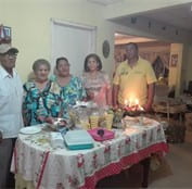 Five people poses next to each other with table in front of them decorated in a festive way and holding various food dishes.