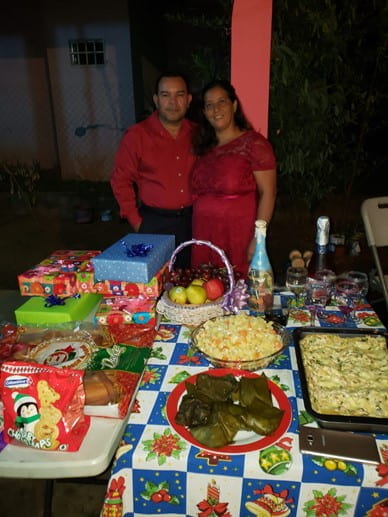 Two people posing next to each other and a large table of food dishes before them.
