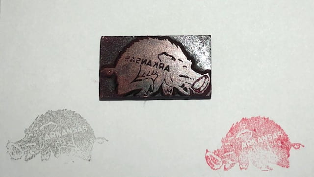 A white paper with a Razorback stamp face-up with two ink illustrations made with it just below - one in black ink and the other in red.