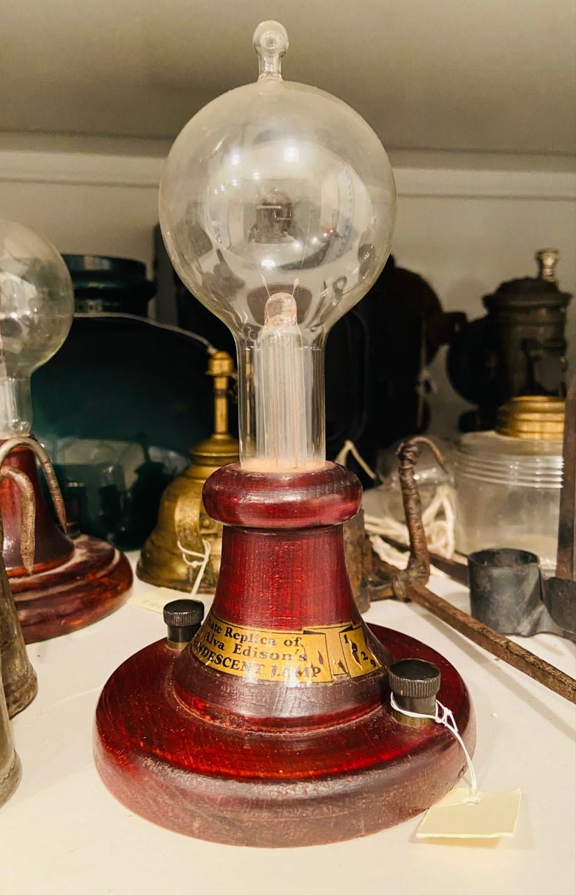 An old-fashioned clear light-bulb on a wooden-based that says "Replica of Thomas Edison's Incandescent Lamp."