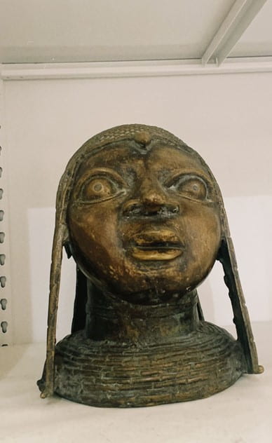 Metal figurine featuring face, neck and shoulders of a person.