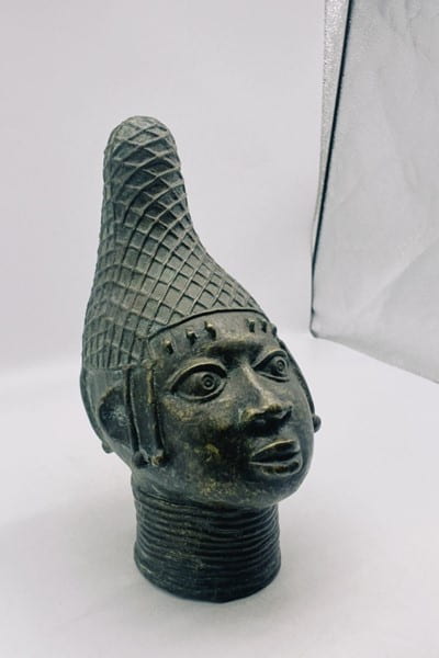 Metal figurine featuring face, neck and shoulders of a person.
